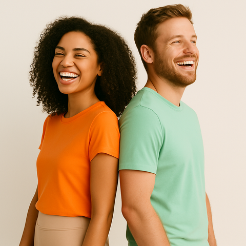IO74 collection. A smiling man and woman stand back-to-back against a neutral background. She wears an orange shirt; he wears a mint green one. The mood is cheerful and relaxed.